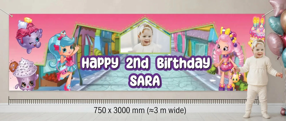 Person standing beside the Shopkins Birthday Banner for scale, with size guide showing 750 x 3000 mm